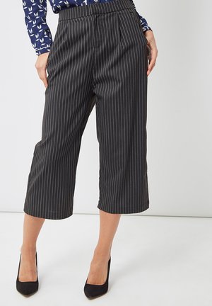 Pantalones cortos negros con rayas verticales blancas, con un frente plisado y una textura suave. Usados con tacones altos negros.