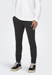 Pantalones jogger de color gris oscuro, fabricados con una tela suave, que presentan un diseño ajustado y una cintura elástica, combinados con zapatillas negras con suelas color crema.