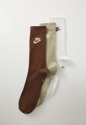 Drei Paar Socken: braun, olivgrün und weiß. Jede hat eine gerippte Textur und ein besticktes Nike-Logo in kontrastierender Farbe oben.