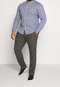 Lichtblauwe lange mouwen shirt met een knoopsluiting bij de kraag, gecombineerd met grijze geruite broek en zwarte sneakers met witte zolen.