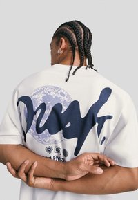 White short-sleeve t-shirt featuring a large navy graphic with a circular design and text on the back. Textured with a relaxed fit.