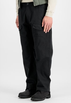 Person wearing black cargo pants with flap pockets and black boots, standing against a plain white background.