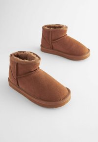 Bottes de cheville marron en daim doux avec doublure en peluche, présentant un embout arrondi, une semelle plate et un design de sangle croisée pour un détail supplémentaire.