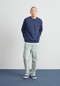 Marineblå sweatshirt med rund hals, lyse vaskede baggy jeans, og sorte og hvide sneakers. Glat tekstur, afslappet pasform, og minimalistisk design.