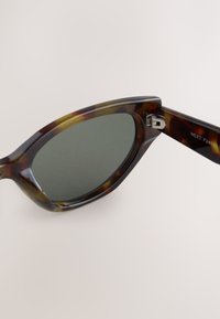 Saulesbrilles ar bruņurupuča raksta ietvaru un tumši zaļiem stikliem, leņķveida kaķu acu formu, pulētu apdari un metāla eņģes detaļu ar gravējumu "NEXT".