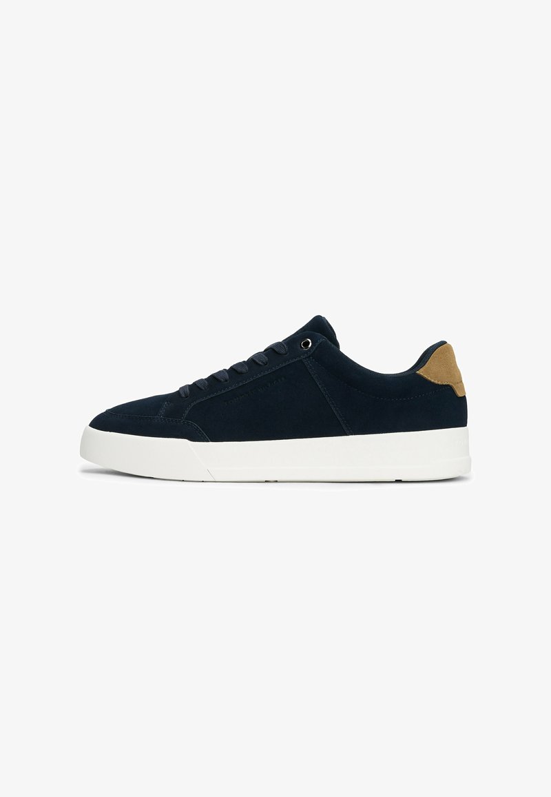 Navy suede sneaker with a white rubber sole, featuring round laces, metal eyelets, and a tan suede accent on the heel.
