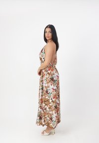 Robe maxi florale en tissu doux, présentant un motif de fleurs multicolores aux nuances de marron, blanc et vert ; design sans dos.