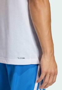 Camiseta blanca de manga corta hecha de material ligero. Presenta una etiqueta de tela transpirable "CLIMACOOL" cerca del dobladillo. Se lleva con pantalones cortos azules.
