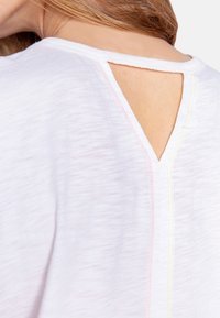 Witte t-shirt met een V-vormige uitsnede aan de achterkant, met contrasterende stiksels in roze en geel. Zachte, lichte stof met een losse pasvorm.