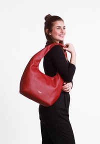Red leather shoulder bag with a large opening, soft texture, and a distinctive cutout handle. Features a silver logo on the front.