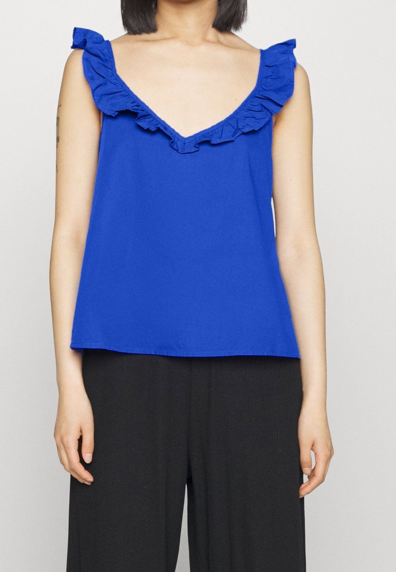 Haut bleu sans manches avec accents de volants le long de l'encolure en V. Confectionné dans un tissu léger, il présente une coupe ample et un design simple.