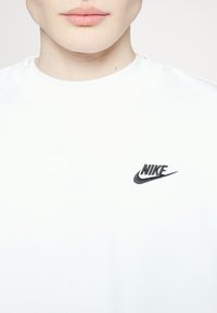 T-shirt en coton blanc avec un logo Nike noir sur la zone gauche de la poitrine. Design simple à col rond avec une texture lisse.