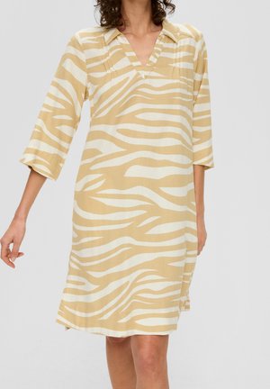 Frau trägt ein beige-weiß gestreiftes, knielanges Kleid mit Zebra-Muster, drei Viertel Ärmel und V-Ausschnitt.