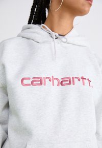Felpa grigia in cotone con tasca a canguro, caratterizzata da un logo ricamato in rosa di grande impatto. Il design include un cappuccio con coulisse.