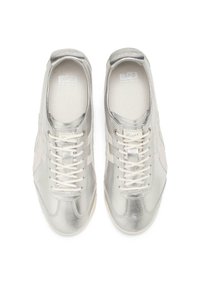 Silvriga metalliska sneakers med en slät yta, som har vita snören och detaljer. Rund tåform, låg design och logotyp på tungan.