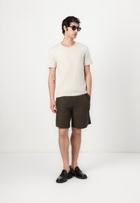 Light beige cotton t-shirt, dark brown linen shorts, and black leather loafers. Accessorized with black sunglasses. Simple, casual outfit.