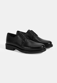 Zwarte leren dresschoenen met een gladde afwerking, ronde neuzen en vetersluiting. Kenmerkt zich door een platte rubberen zool en minimale stikseldetails.