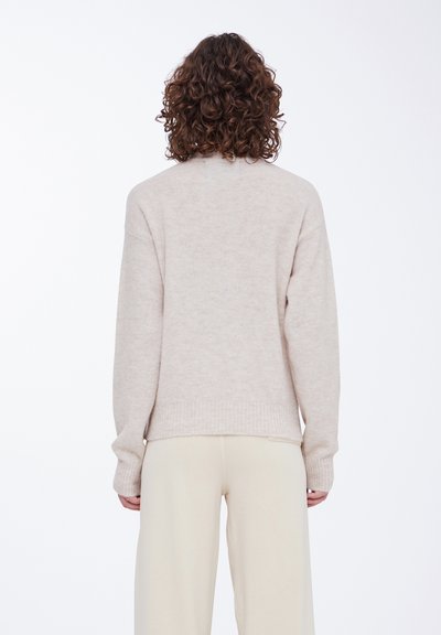 Beige strikket sweater med ribbede manchetter og kant, der har en blød tekstur og en afslappet pasform, set bagfra mod en hvid baggrund.