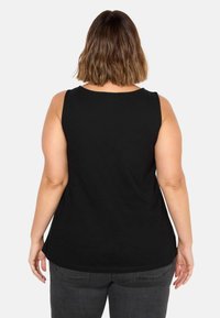 Schwarzes ärmelloses Oberteil aus weichem Stoff, mit einem gerundeten Halsauschnitt und einer lockeren Passform. Sichtbare Nähte entlang des Saums und der Schultern.