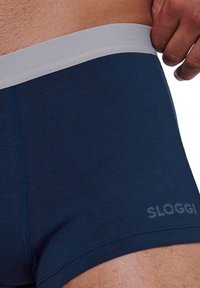 Tummansiniset SLOGGI bokserit ovat varustettu vaalean harmaalla joustavalla vyötärönauhalla. Kangas on sileä, muotoiltu ja siinä on huomaamattomia ompelutietoja.