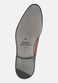Semelle de chaussure en caoutchouc noir et cuir gris clair, comportant le nom de la marque "Henry Stevens" et la taille "8", avec cinq clous métalliques visibles et une texture lisse.