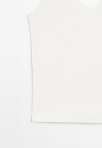 Bílá bezrukávová cami s designem ve tvaru V, vyrobená z hladkého, jemného materiálu, s čistými okraji a minimalistickým stylem.
