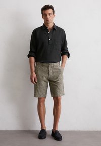 Schwarzes Leinenhemd mit Kragen und Knopfdetails, kombiniert mit beigen gestreiften Shorts und dunklen Mokassins, was ein lässiges Ensemble schafft.