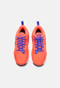 Κόκκινα αθλητικά παπούτσια με επάνω από πλέγμα, μπλε κορδόνια και μαύρες λεπτομέρειες. Ο σχεδιασμός περιλαμβάνει τρύπες και ένα λουρί στη φτέρνα για εύκολη χρήση.