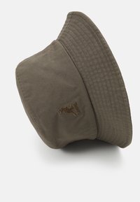 Sombrero tipo bucket hecho de algodón verde oliva duradero con un ala texturizada y detalle de logo bordado. Forma suave y estructurada con una cúpula ancha.