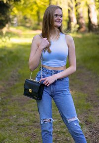 Borsa nera in similpelle con hardware dorato, design a scatola e tracolla a catena. Indossata con una canotta corta blu chiaro e jeans strappati a vita alta.