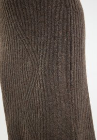 Tissu en maille marron avec des côtes verticales et un motif texturé, présentant une apparence douce et chaleureuse. Détails avec des variations tonales subtiles.