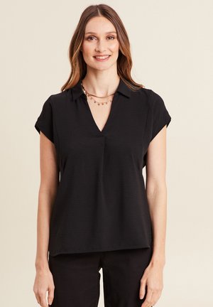 Blouse noire à manches courtes avec un décolleté en V, présentant une texture subtile et une coupe décontractée. Portée avec un collier en or à plusieurs couches.