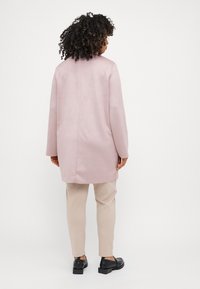 Light pink, long coat with a smooth texture, featuring a straight cut and minimal seams, paired with beige trousers and black shoes.
