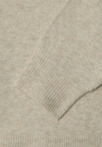 Ljusbeige tröja med en mjuk, strukturerad stickning, ribbade muddar och en lätt melerad finish som framhäver subtila färgvariationer.