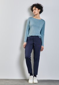 Hellblaues Langarmoberteil aus weichem Material; marineblaue Cargo-Hosen mit seitlichen Taschen und elastischen Bündchen; weiße Sneaker runden das Outfit ab.