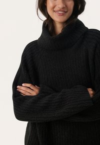Zwarte, getextureerde oversized trui met een hoge kraag en brede mouwen. Heeft een geribbelde patroon, wat zorgt voor een gezellige uitstraling.