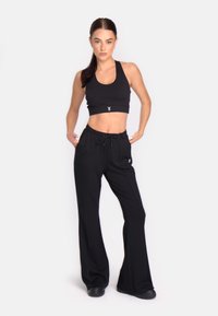 Top scurt negru și pantaloni cu talie înaltă dintr-un material moale, având un cordon la talie și un logo minimalist pe față.