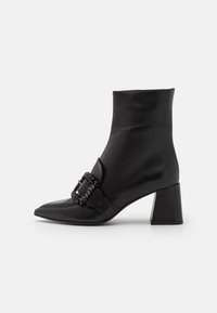 Bottines en cuir noir avec un bout pointu, détail de boucle décorative et un talon épais. Texture lisse et design élégant.