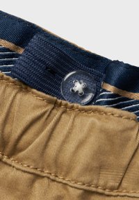 Bežna tkanina pas s modrimi akcenti, ki vključuje prozoren plastični gumb in šivane detajle. Delno vidna črtasta podloga.