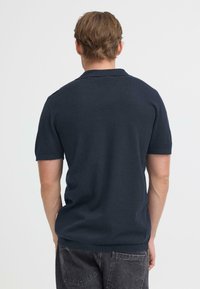 Polo bleu marine à manches courtes, fabriqué en tissu lisse, doté d'un col classique et d'une finition texturée subtile. Design simple et ajusté.