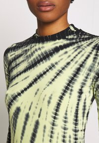 Dlouhý rukáv top v světle zelené barvě s černým tie-dye vzorem, se stojáčkem a žebrovaným lemem u límce. Hladká textura.