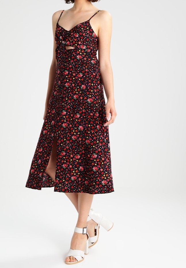 Blommig midiklänning i svart med justerbara spaghetti-band, en knutdetalj fram och en sidslits. Matchad med vita klacksandaler.