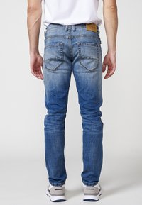 Vaqueros de mezclilla azul de corte ajustado con efecto desgastado, que presentan un parche de piel de la marca en la cintura y dos bolsillos traseros con solapas puntiagudas.