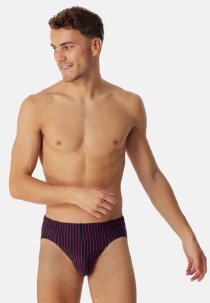 Costume da bagno slip blu navy con righe verticali rosse, tessuto elasticizzato e design aderente. Texture liscia e vita elastica per il massimo comfort.