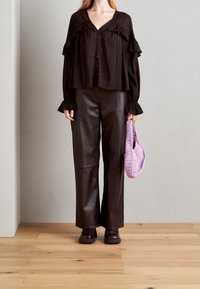 Sort bluse med voluminøse detaljer, knappet fortil og lange ærmer, parret med brun læderbukser med høj talje og en lille lilla hæklede taske.