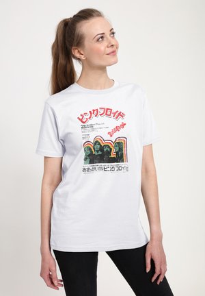 Frau mit Pferdeschwanz, die ein weißes T-Shirt mit bunter Vintage Pink Floyd-Grafik und japanischem Text trägt und leicht nach oben und zur Seite schaut.