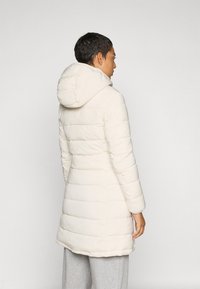 Puffer, knie-lange jas in off-white, met een capuchon en horizontale quilting. De stof lijkt glad met een licht glanzende textuur.