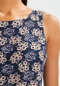 Marinblå blomsterklänning med rundad halsringning, prydd med blommönster i beige, vitt och lila, tillverkad av ett mjukt tyg.