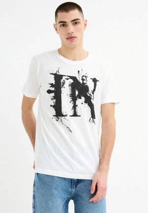 Camiseta de algodón blanca con un gran diseño gráfico negro con acentos de salpicaduras. Mangas cortas, escote redondo y corte relajado.