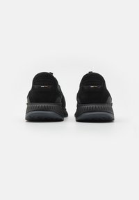 Svarta sportskor med en texturerad mockaöverdel, utrustade med vadderad krage, bakre dragflik och kontrasterande häl-detalj. Böjd gummisula.
